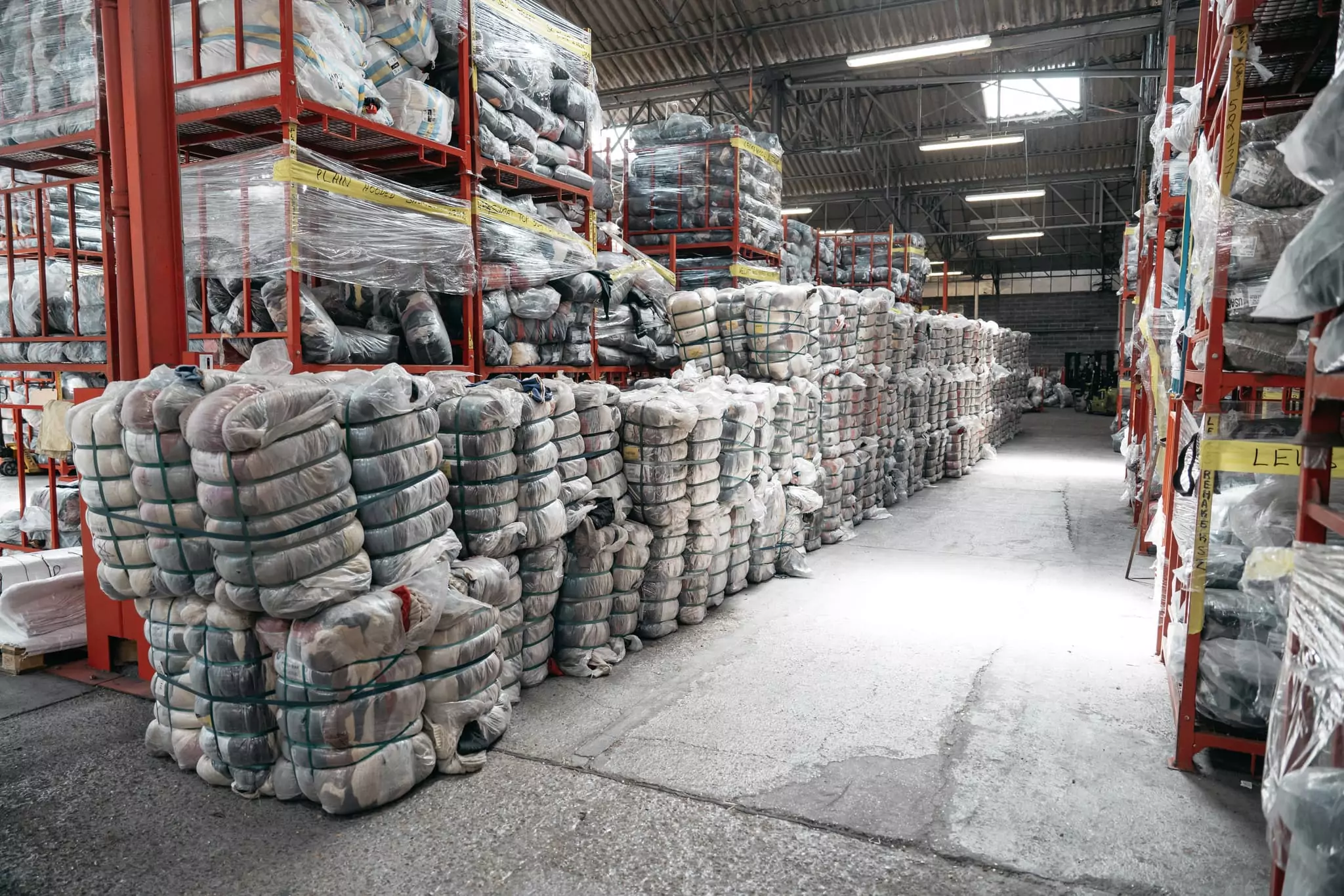 Balles de vêtements vintage cerclées et empilées devant des racks de stockage dans l'entrepôt