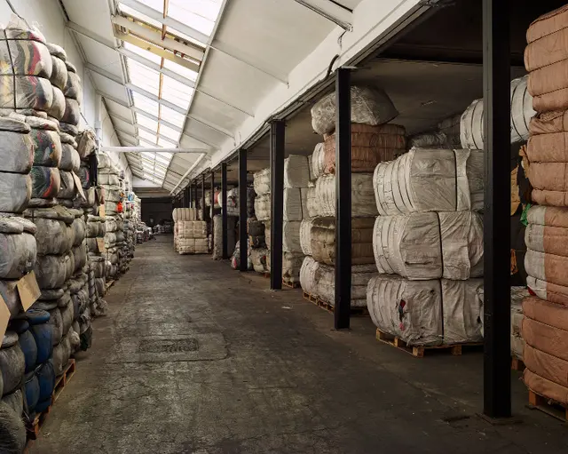 Entrepôt Eureka Fripe allée de balles de vêtements vintage stockées sur palettes Normandie